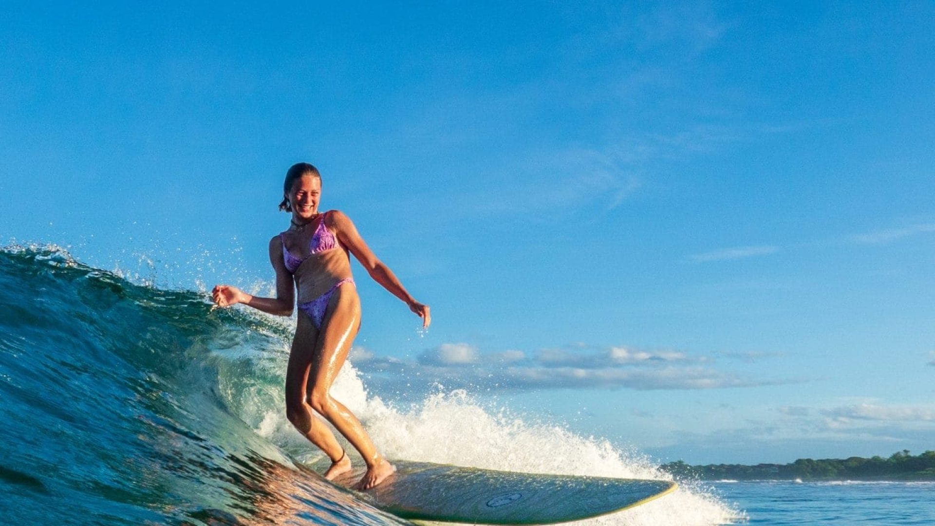 Girl surfing on ocean wave with clear blue sky in background, summer fun.