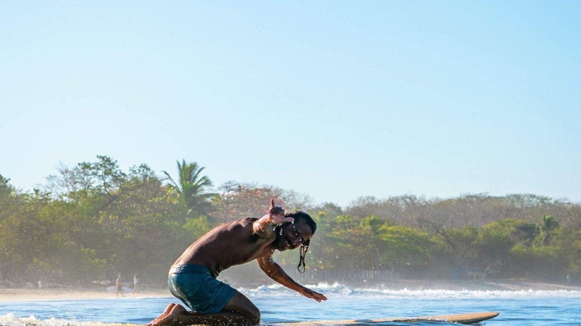 Surfing lifestyle on a sunny beach with clear blue skies and tropical greenery.