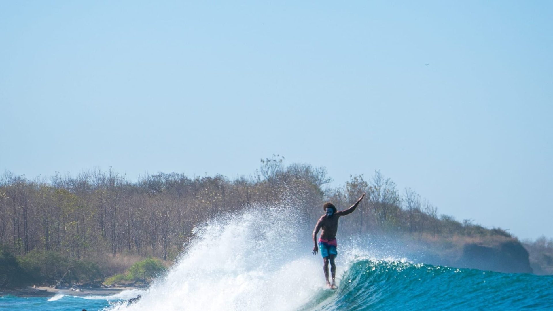Vibrant surfer riding a blue wave in a tropical ocean setting, showcasing surfing, beach lifestyle, and water sports.