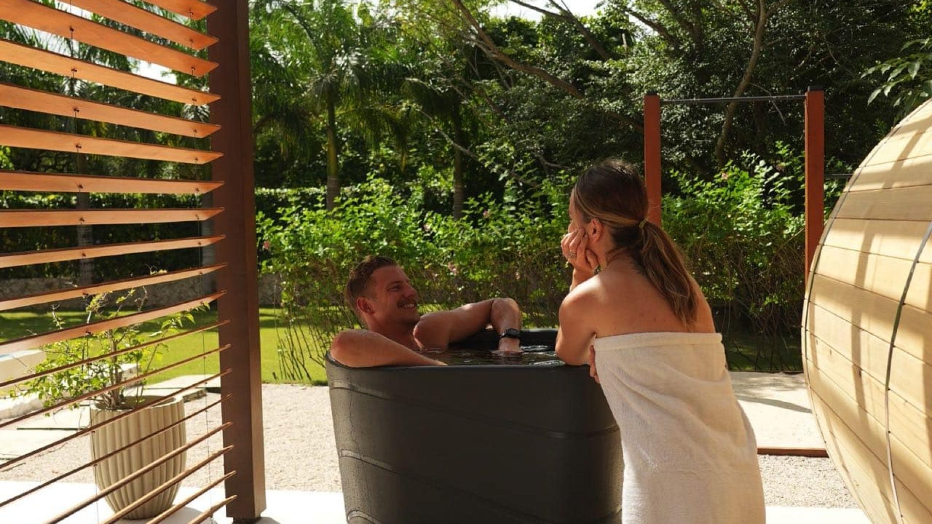 Relaxing outdoor hot tub with two people enjoying a sunny day in a lush green garden, tropical ambiance, Vida Pinilla experience.