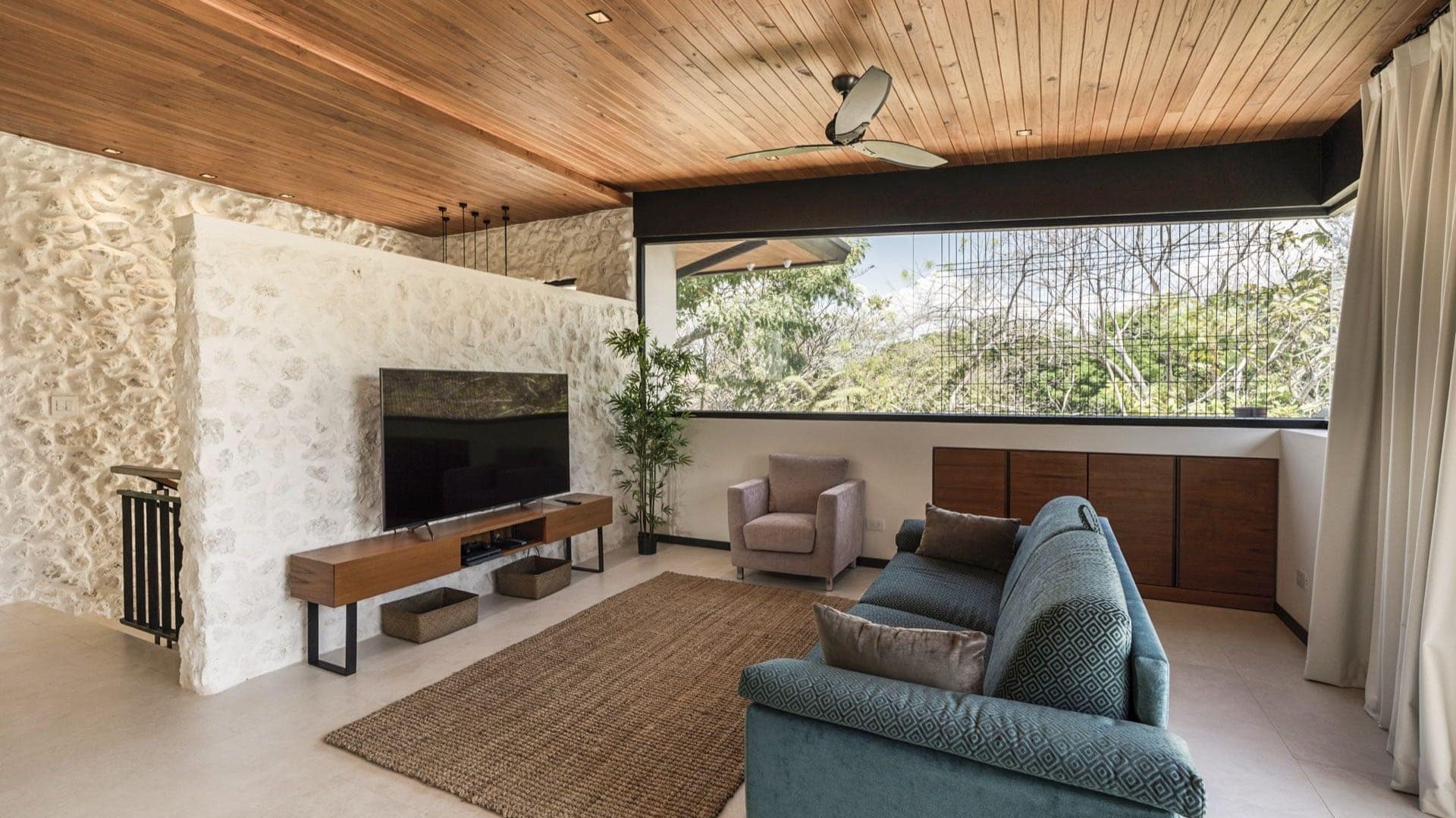 Modern living room with stone wall, wooden ceiling, large window, and comfortable furniture.