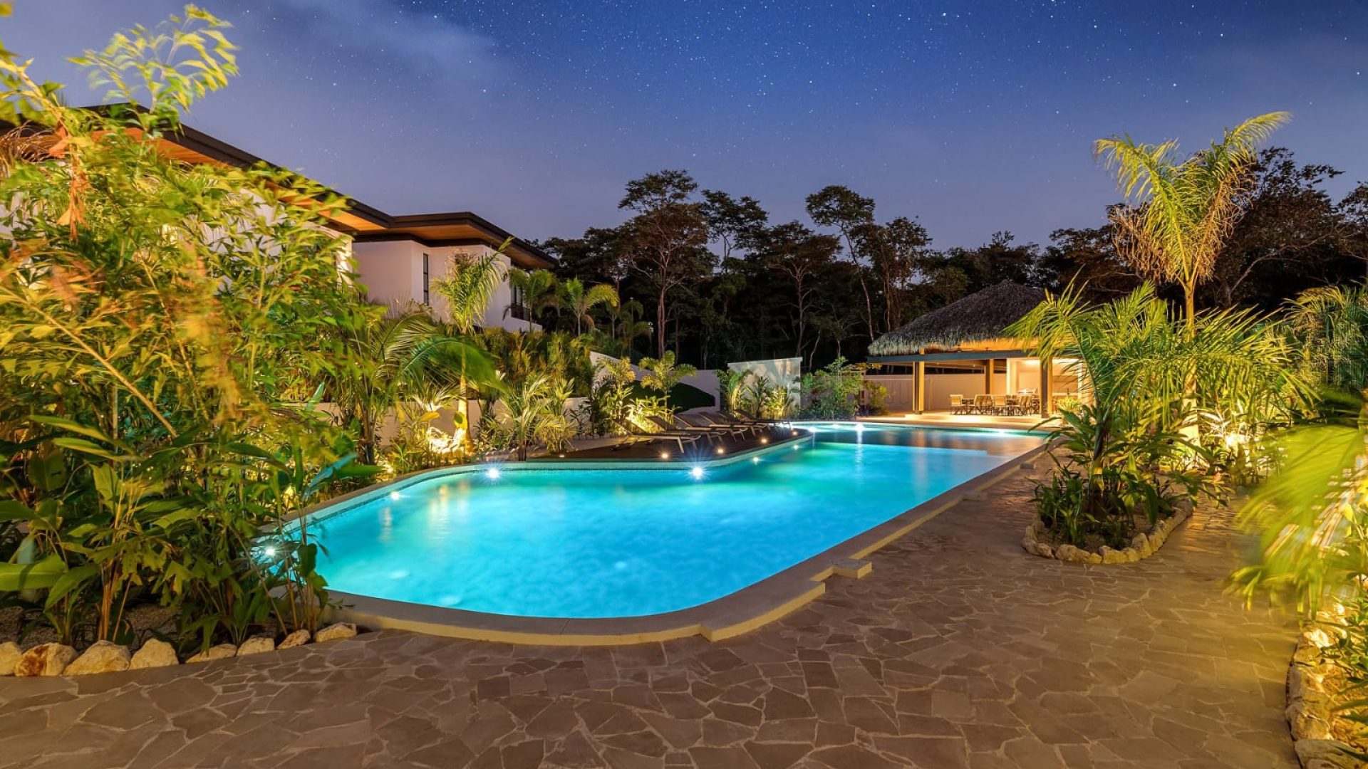Relaxing nighttime view of a illuminated outdoor swimming pool surrounded by lush tropical plants at Vida Pinilla resort.