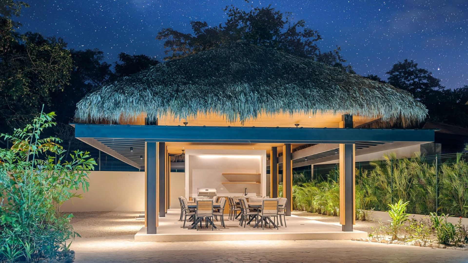 Modern outdoor patio with thatched roof, poolside lounge, and lush tropical landscaping at Vida Pinilla.