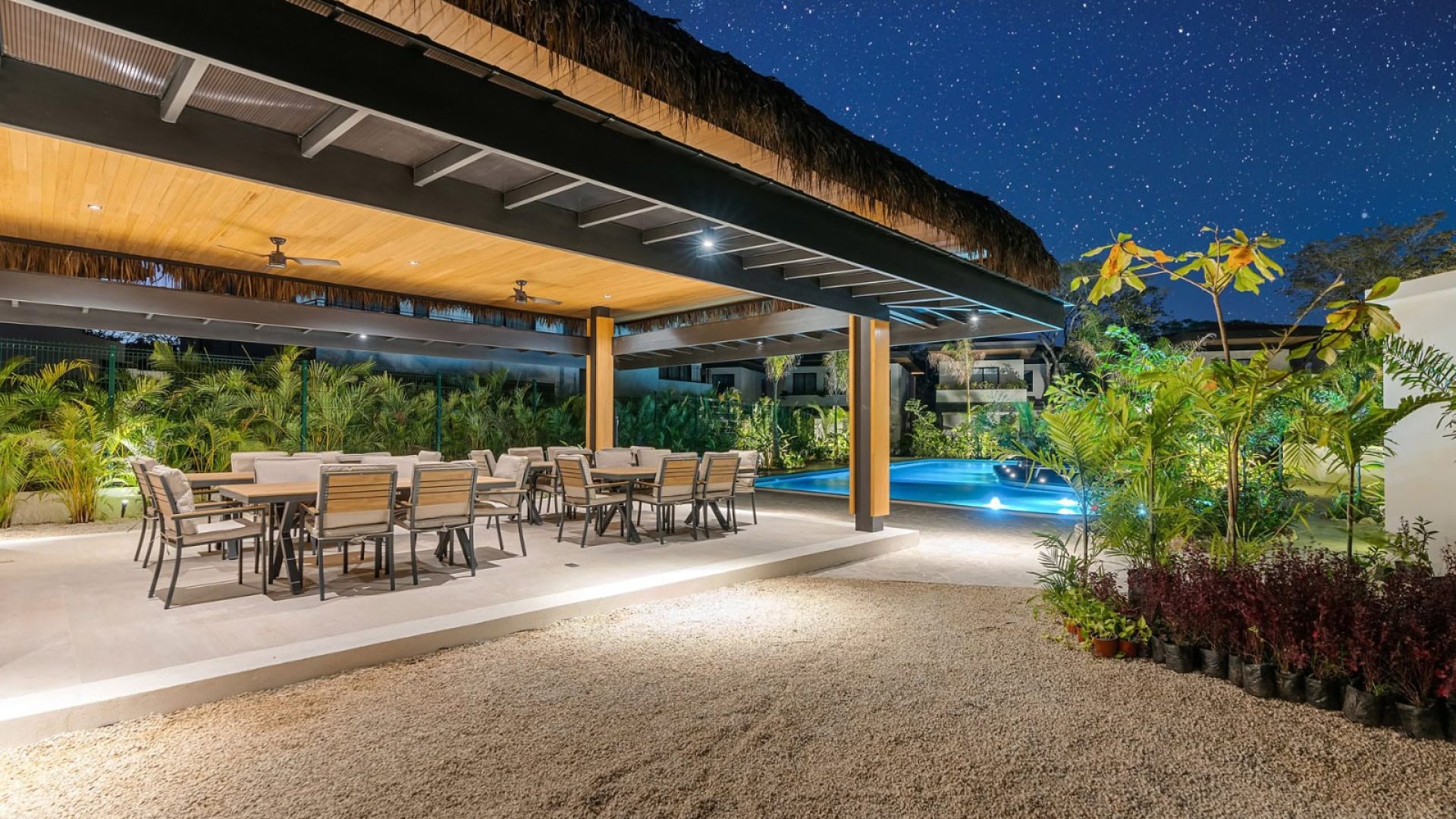 Modern outdoor pool area with dining space and lush tropical landscaping at Vida Pinilla resort at night.