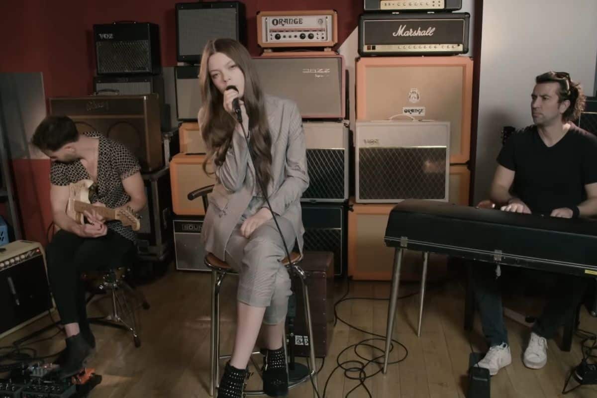 Young woman singing with band in music studio with amps and instruments.