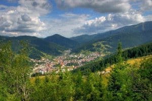 Панорамна гледка към малък планински град, заобиколен от гъсти гори и хълмове при ясно небе.