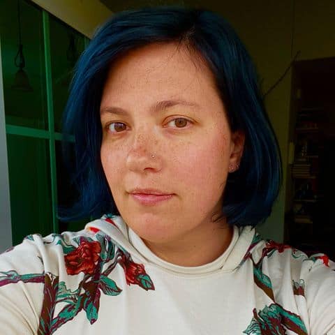 Colorful portrait of a young woman with blue hair taking a selfie indoors, showcasing contemporary art style and vibrant personality at Visual Arts Passage exhibition.