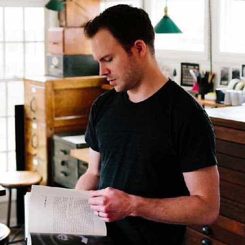 A contemplative man reading a book in a cozy, artsy cafe with natural lighting, wooden decor, and creative workspace elements, embodying the inspiring environment of Visual Arts Passage.