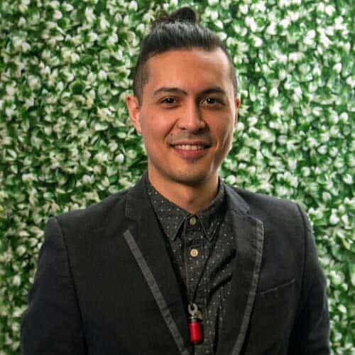 Portrait of a confident man at Visual Arts Passage with a lush green floral backdrop showcasing contemporary art and vibrant local culture.