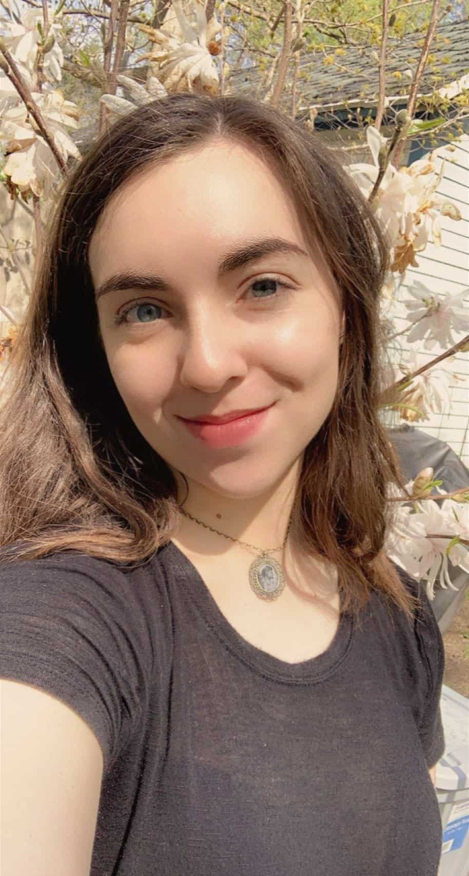 Beautiful young woman taking a selfie outdoors with blooming trees in the background, showcasing modern portrait photography at Visual Arts Passage.