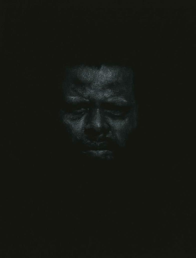 A dark, textured sculpture of a human face emerging from a black background, emphasizing contemporary art and mixed media artistry.
