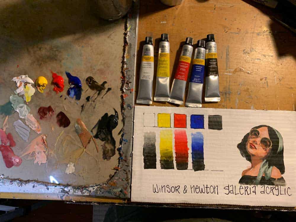 Vibrant oil paint tubes, a color swatch chart, and a portrait of a woman with sunglasses on an artist's palette evoke creative processes at Visual Arts Passage.