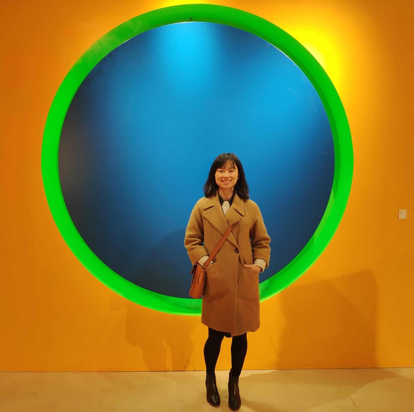Vibrant abstract art installation with a colorful circular frame and a woman standing in front, highlighting modern art exhibits at Visual Arts Passage in an art gallery setting.