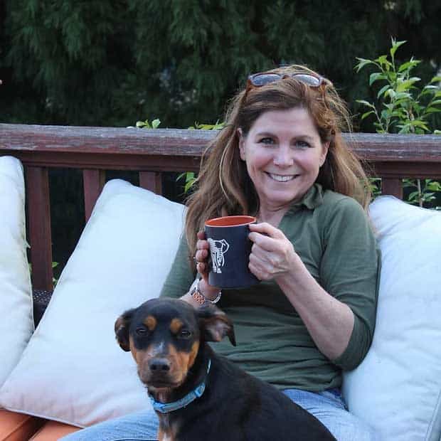 Relaxing woman enjoying coffee outdoors with her dog on a patio, showcasing leisure and outdoor lifestyle.