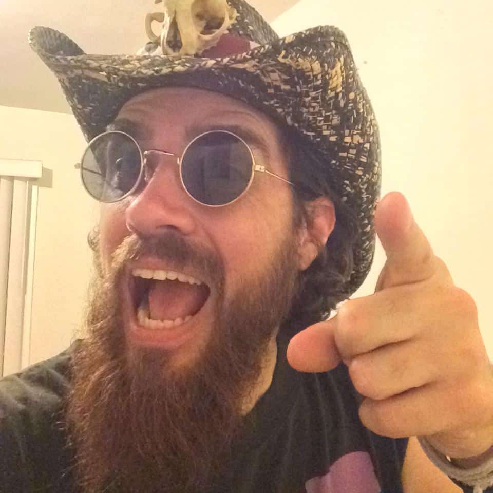 Colorful man dressed in a cowboy hat and sunglasses, smiling and pointing with enthusiasm, showcasing vibrant personality and engaging attitude for artistic and creative expression.