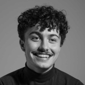 Smiling young man with curly hair in black turtleneck, portrait.