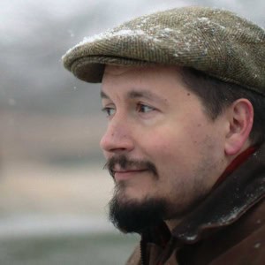 A close-up of a man wearing a wool cap, outdoors in a natural setting, showcasing human expression and detail in portrait photography.
