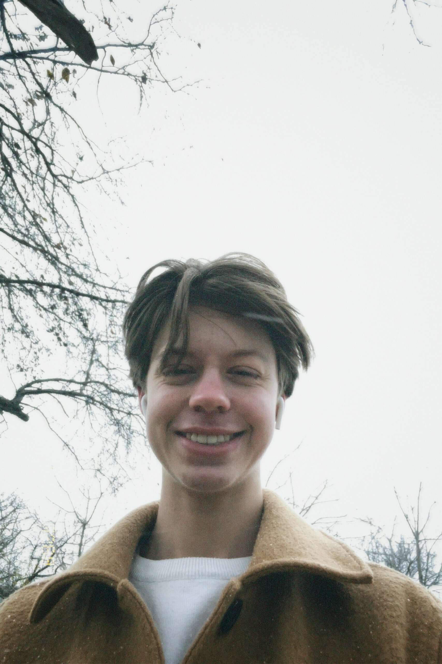 Autumnal portrait of a young smiling person outdoors with trees in background.