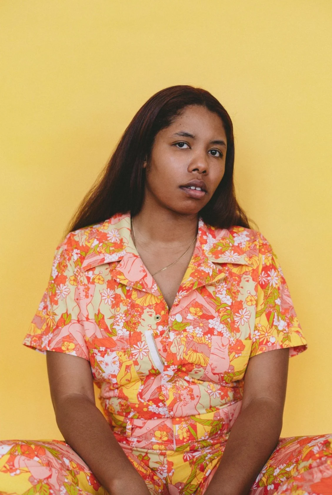 Vibrant portrait of a young woman in colorful floral patterned outfit against a solid yellow background, emphasizing contemporary art and fashion photography.