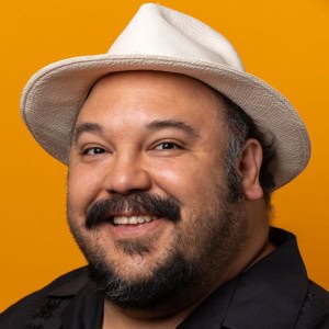 Portrait of a smiling man wearing a white hat against a vibrant yellow background, capturing the essence of contemporary portrait photography and artistic expression on Visual Arts Passage.