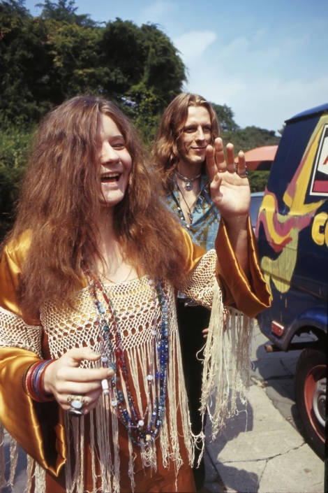 A candid shot of two women with bohemian fashion, smiling and waving outdoors on a sunny day, showcasing vibrant clothing and accessories.