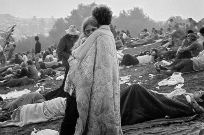 Black and white photo of refugees at a camp, showing people resting and socializing amidst tents and makeshift shelters, capturing the human aspect of displacement.