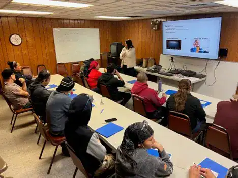 In a class setting, an educator stands in front of two rows of Wisconsin Aluminum Foundry workers, with a screen projecting an English lesson.