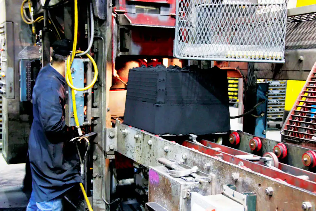 Green sand mold coming down production line, operated by a molder wearing protective clothing.