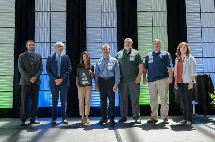 Posed on an awards stage, from left, are Ryan Burzinski of judging committee and Schneider National, Wisconsin Gov. Tony Evers, Michelle Szymik of Wisconsin Aluminum Foundry, Gregg Rabe of Wisconsin Aluminum Foundry, Shane Chase of Wisconsin Aluminum Foundry, Scott Chervenka of Wisconsin Aluminum Foundry, Lisa Smith of award sponsor Keystone Partners.