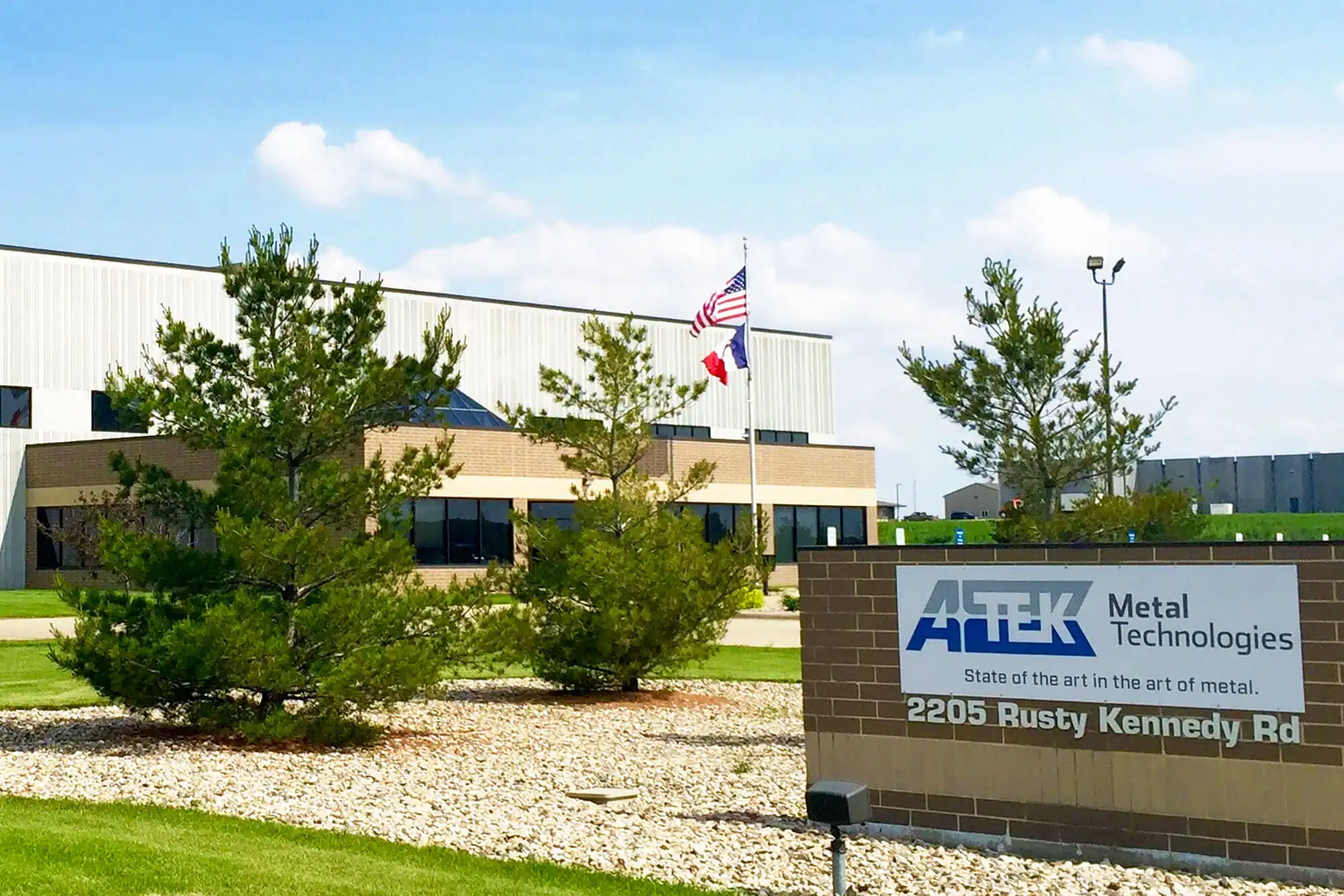 Exterior brick sign with ATEK Metal Technologies in front of the company's headquarters facility with flagpole.
