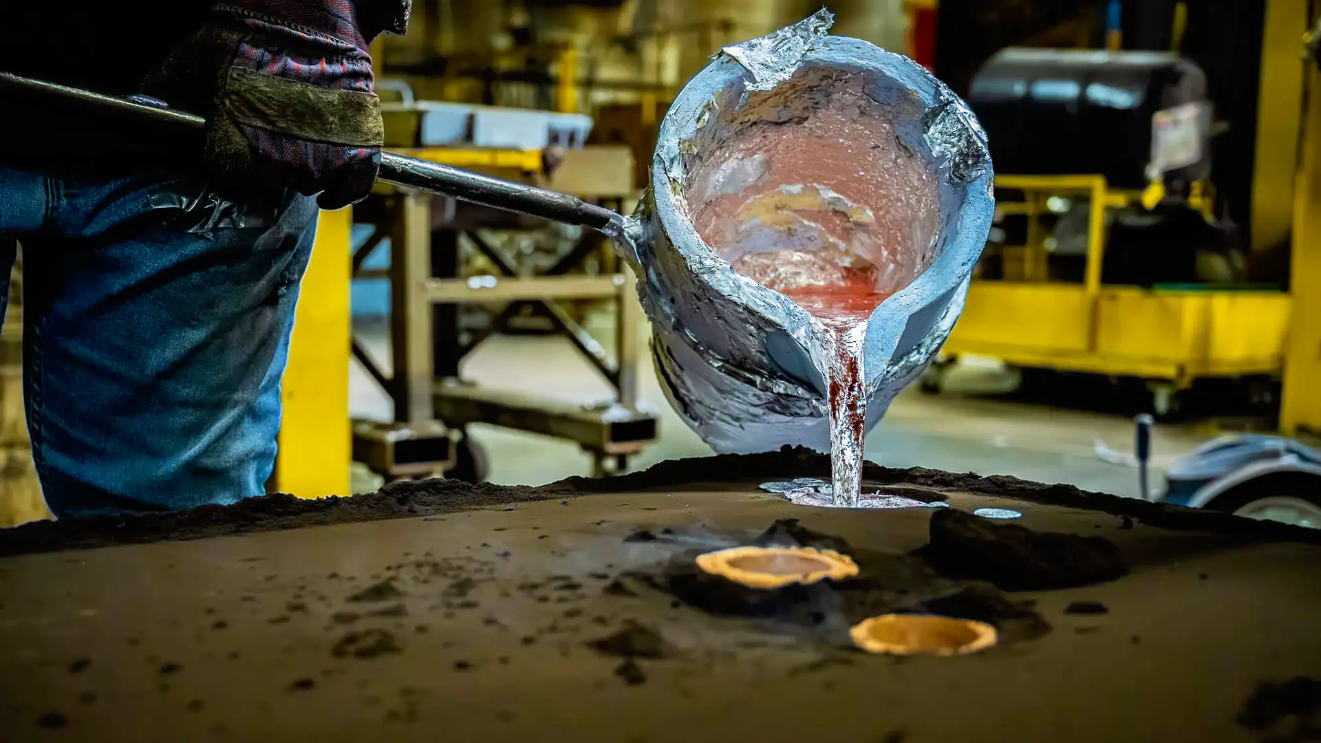 Worker pours a ladel of melted aluminum into large green sand mold.