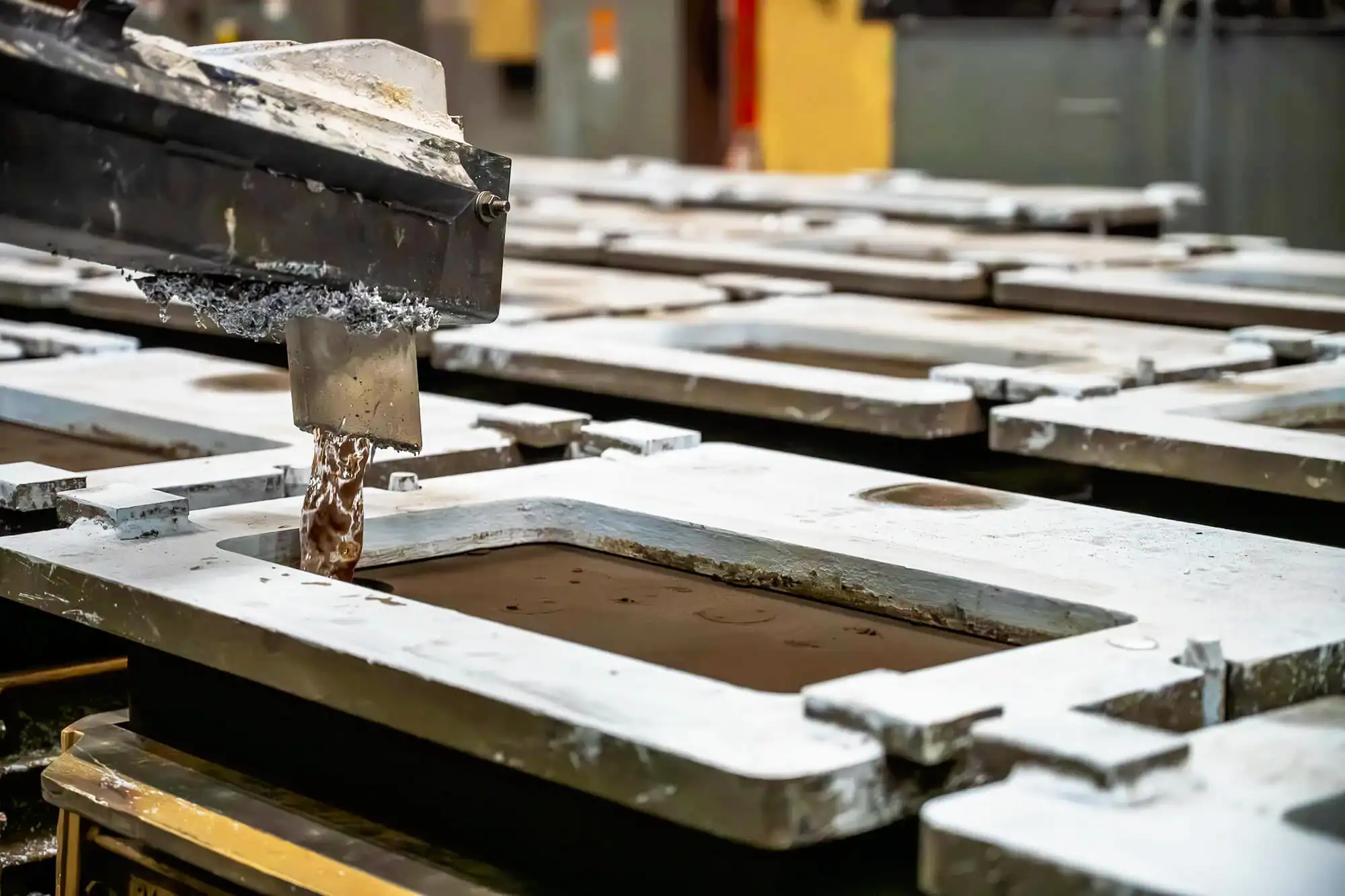 Aluminum pours from a spout to fill one of the green sand molds set up in rows.