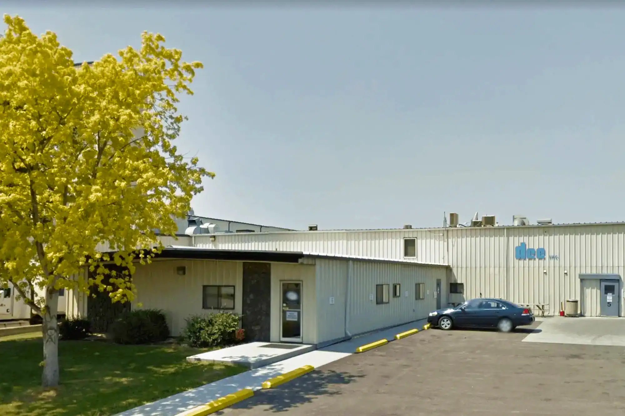 Exterior Dee Manufacturing with view of main office and parking lot with tree out front and casting facility building in background.