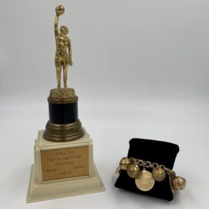 A gold trophy commemorating the history of women's basketball next to a gold bracelet. A gold trophy commemorating the history of women's basketball next to a gold bracelet.