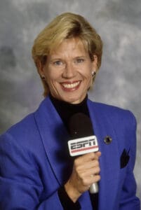 A woman in a blue jacket holding a microphone discussing the history of women's basketball. A woman in a blue jacket holding a microphone discussing the history of women's basketball.