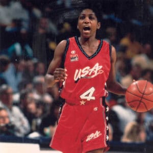A woman in a red uniform, a pioneer in the history of women's basketball, holding a basketball. A woman in a red uniform, a pioneer in the history of women's basketball, holding a basketball.