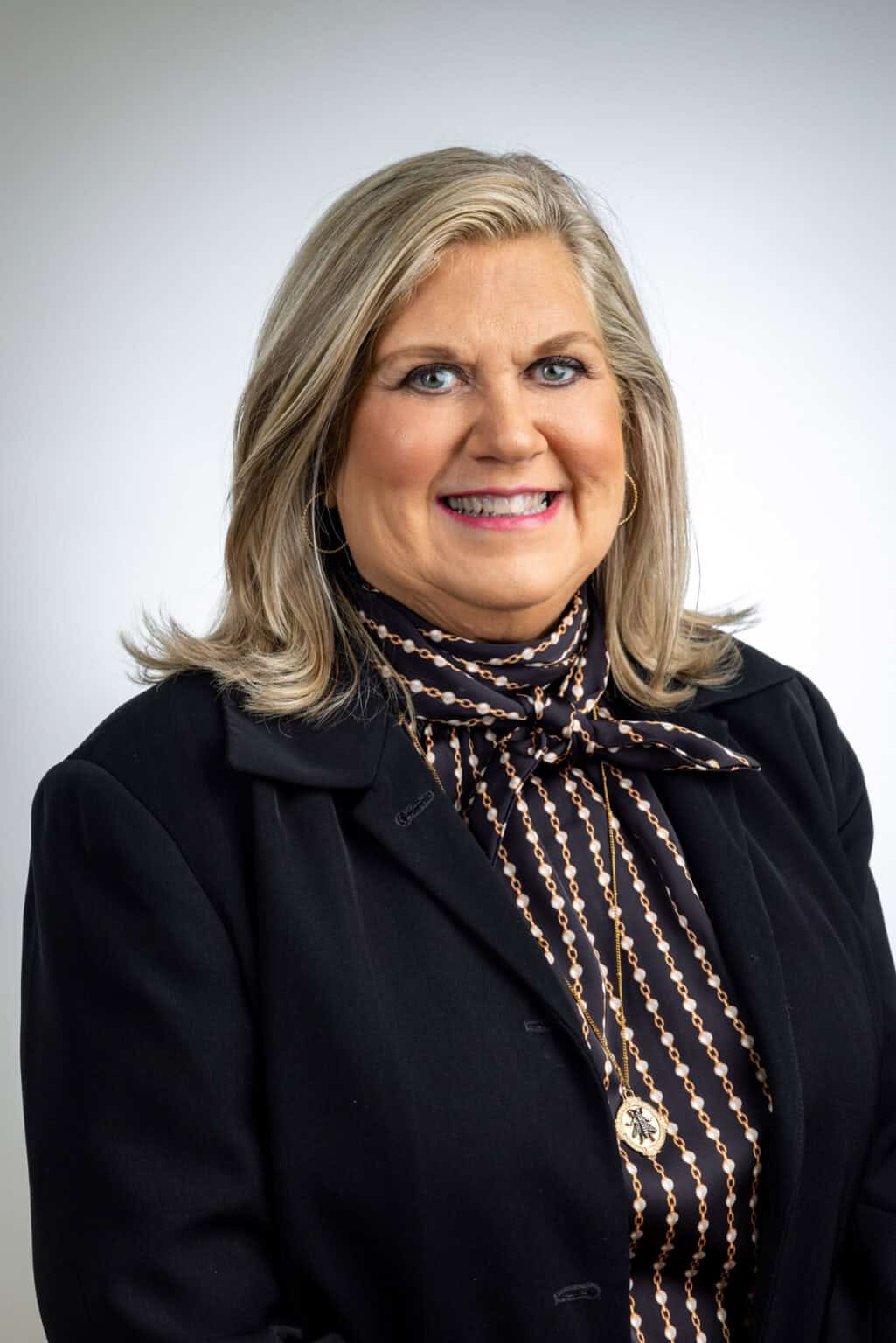 A woman in a black jacket and patterned shirt, who is a Women's Basketball Hall of Fame staff member, is smiling. A woman in a black jacket and patterned shirt, who is a Women's Basketball Hall of Fame staff member, is smiling.