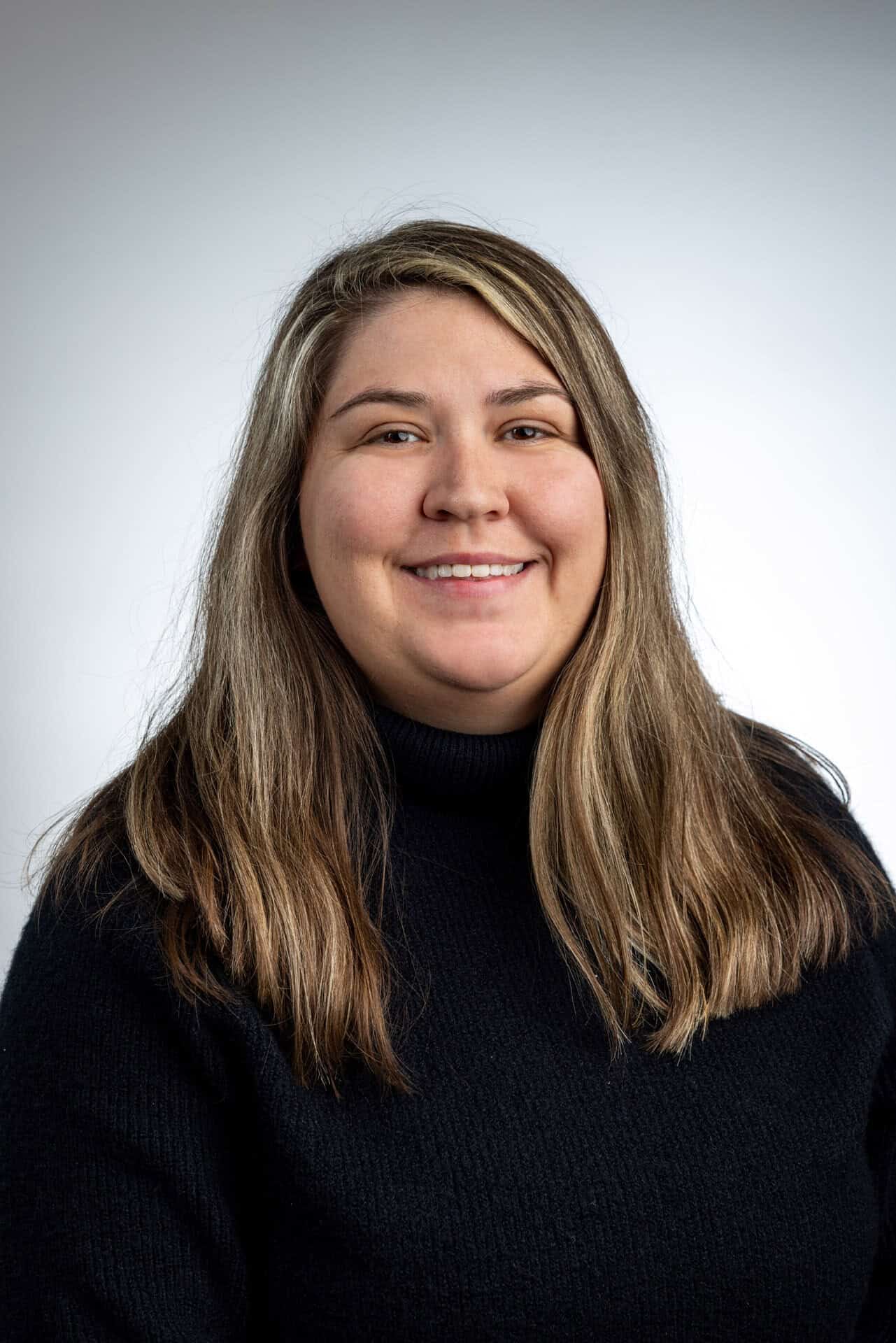 A smiling woman in a black turtleneck shirt, who is a Women's Basketball Hall of Fame staff member. A smiling woman in a black turtleneck shirt, who is a Women's Basketball Hall of Fame staff member.