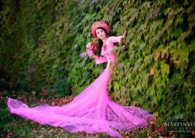 A woman in a pink dress is leaning against a tree.