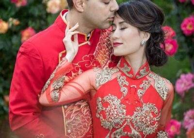 CineCrown Vietnamese couple in red traditional clothing embracing in front of roses.