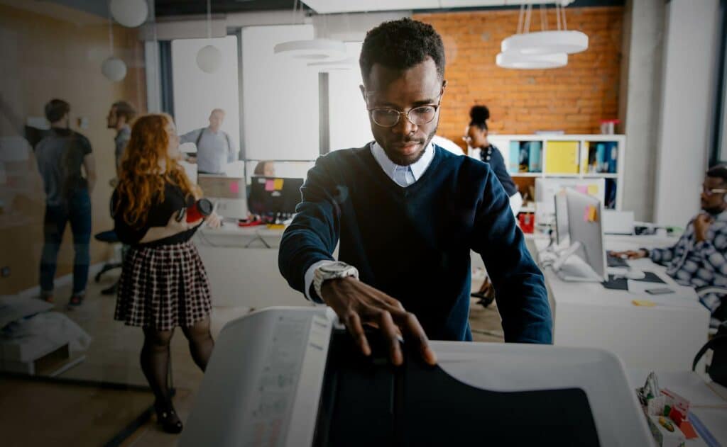 High-tech office with diverse team working on printers and computers at West X Business Solutions center.