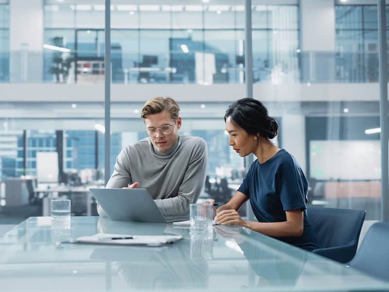 Two employees in aboard room working on a laptop to solve a problem