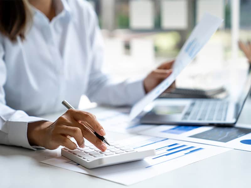 Business professional analyzing financial data with calculator and documents at modern office - West X Business Solutions.