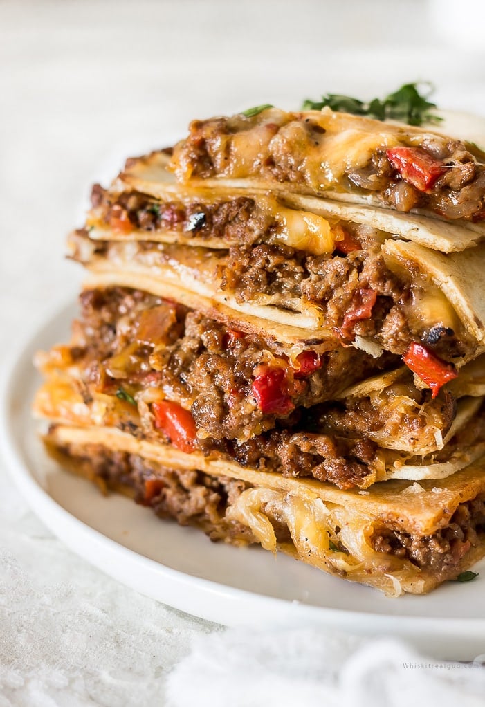 Sheet pan quesadillas that are stacked on top of one another with cheese, peppers and taco seasoning