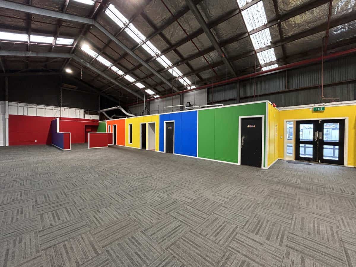 Colorful modular office units inside an industrial warehouse with high ceilings.