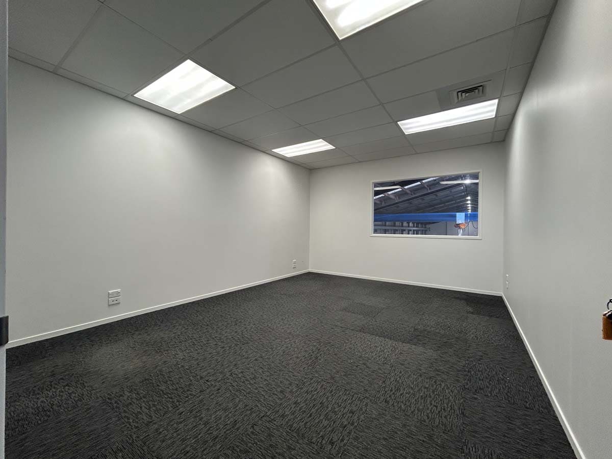 Empty commercial office room with white walls, ceiling lights, and window.