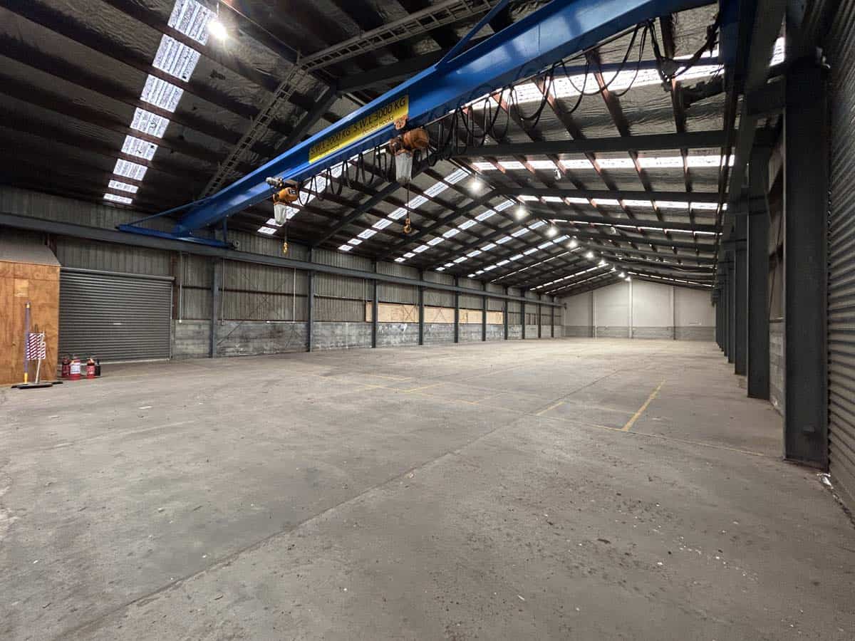 Interior view of a spacious industrial warehouse with high ceilings and overhead crane.