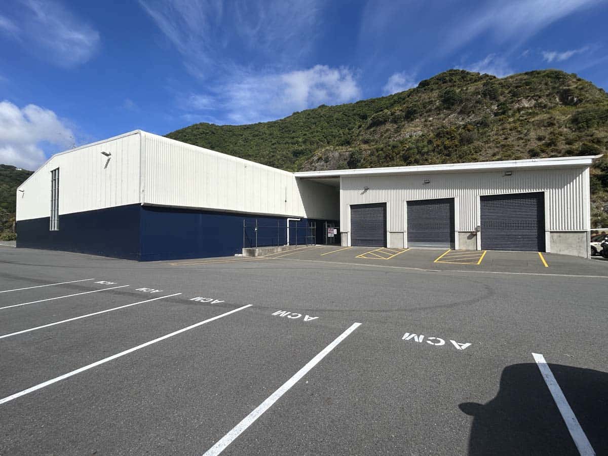 Modern white and navy industrial warehouse with parking at 14 Tyers Road, set against green hills.