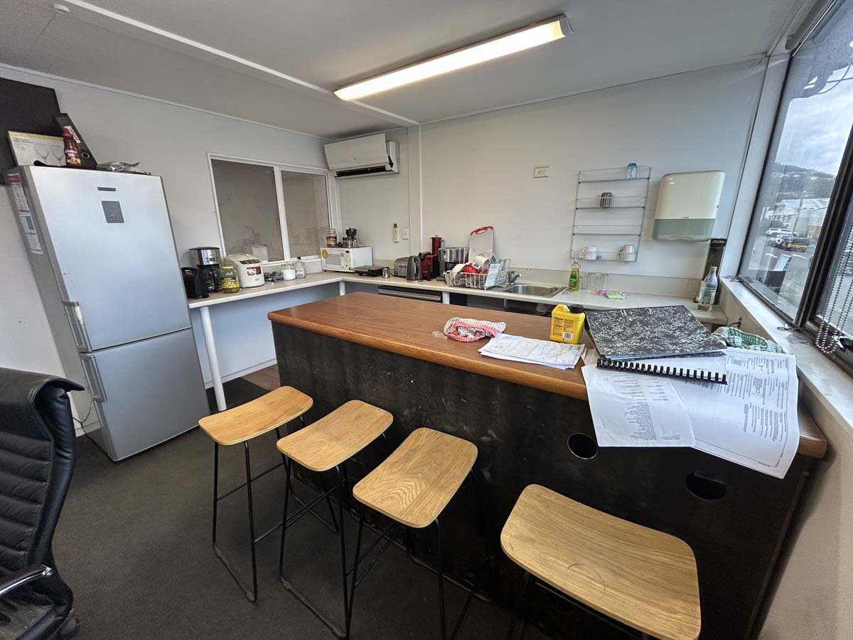 Interior view of a contemporary office kitchen with a breakfast bar, stools, and appliances.