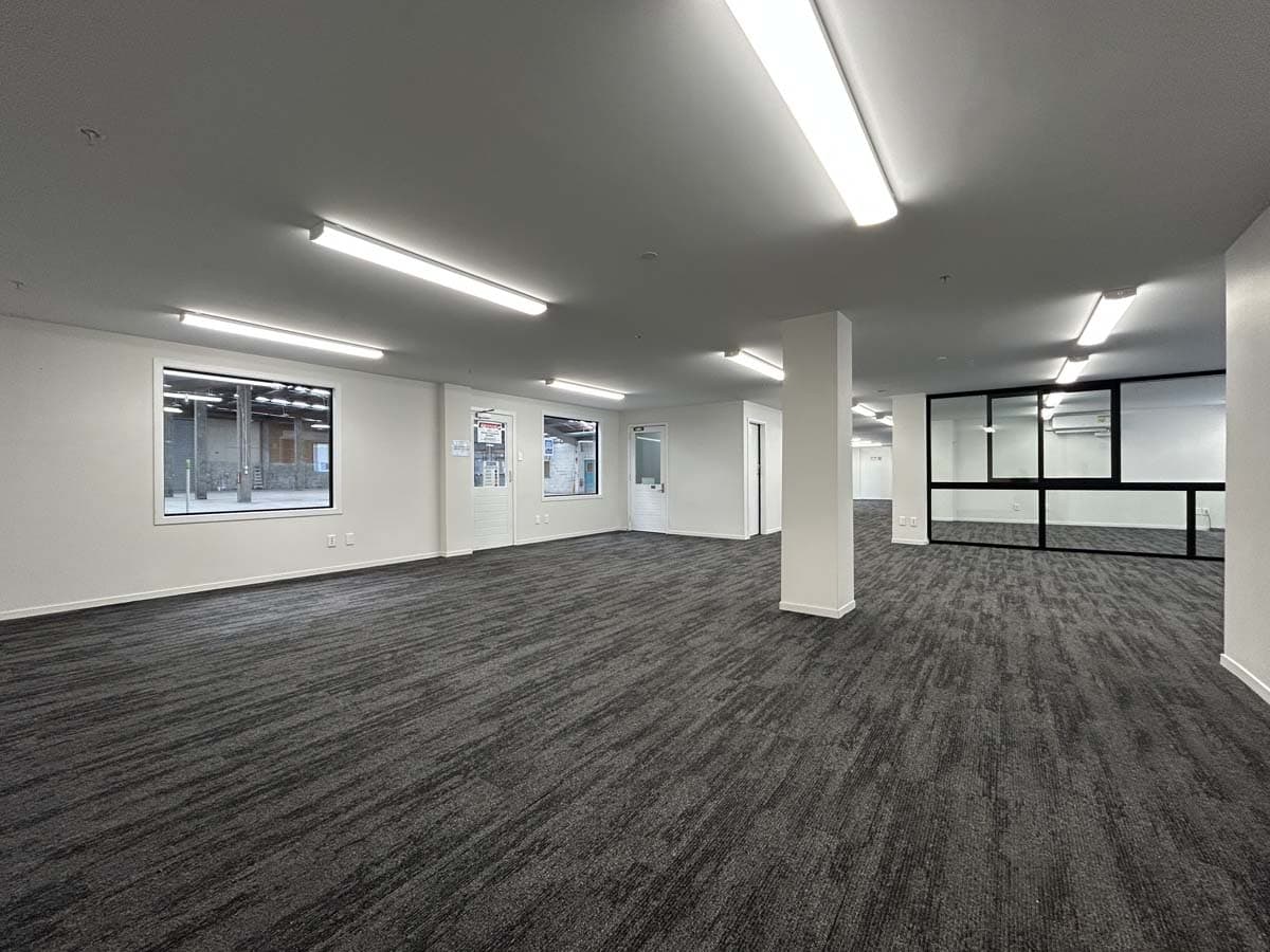 Interior view of a spacious, well-lit office with large windows and carpeted floors.